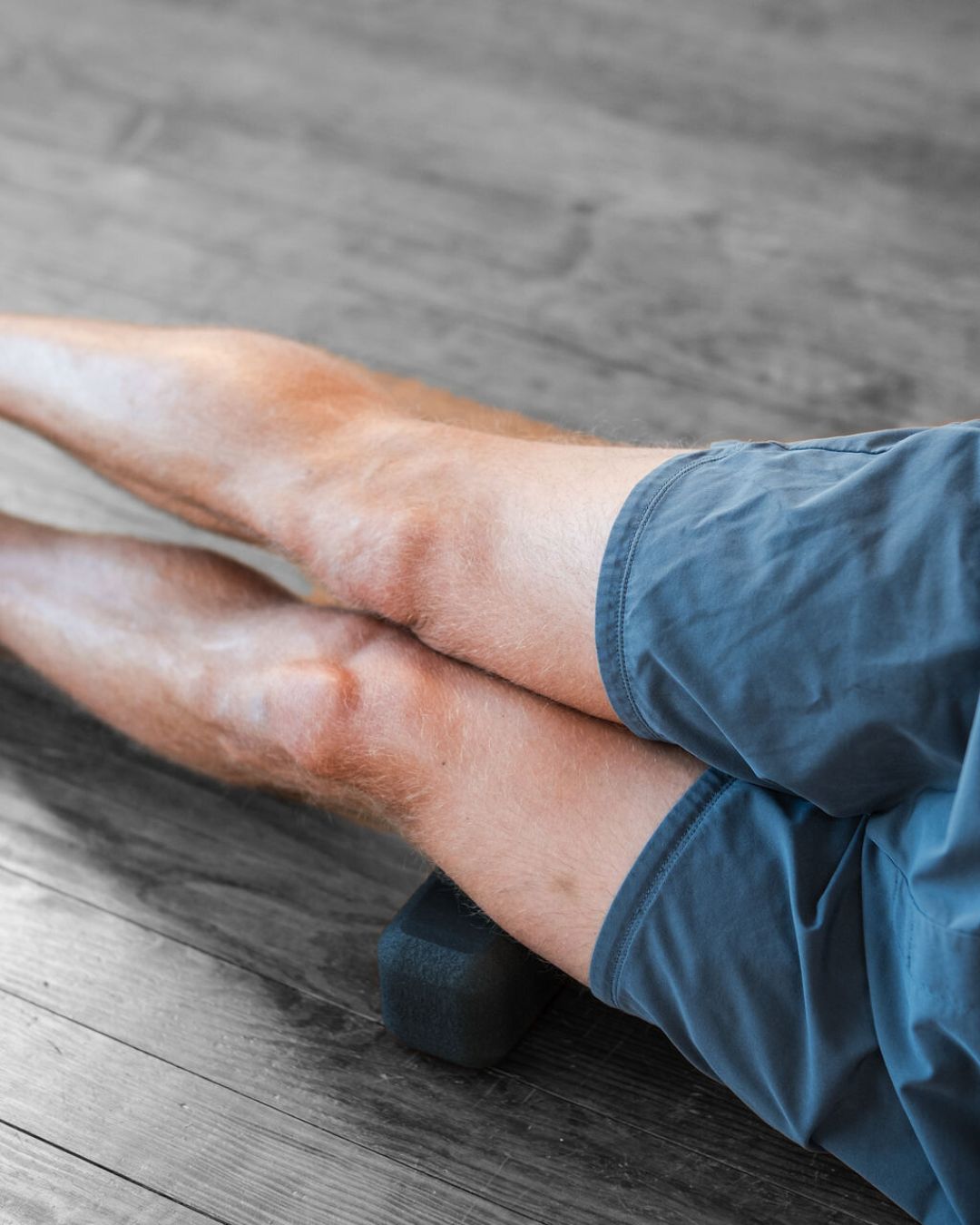 person using a foam (un)Block on the side of their thigh IT band area on a wood floor